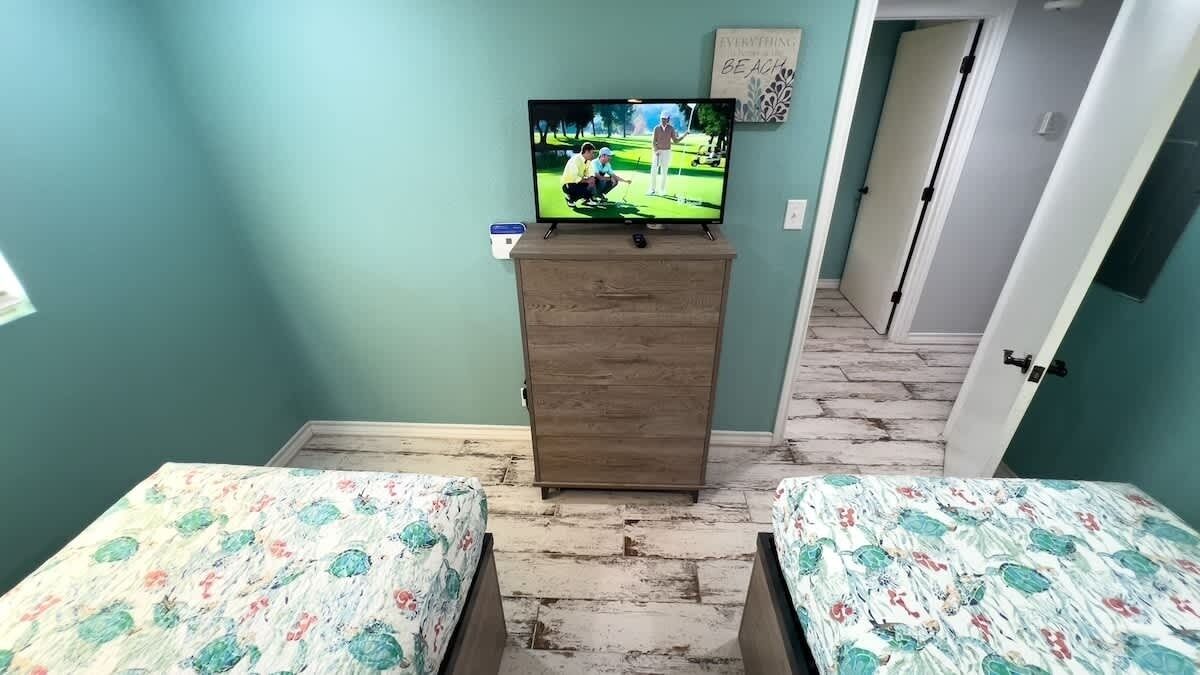 Een kamer met twee bedden, een houten dressoir en een televisie erboven.
