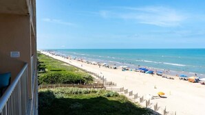 Ein Strand mit Sonnenschirmen und Menschen, ein klarer Himmel und Blick auf den Ozean.