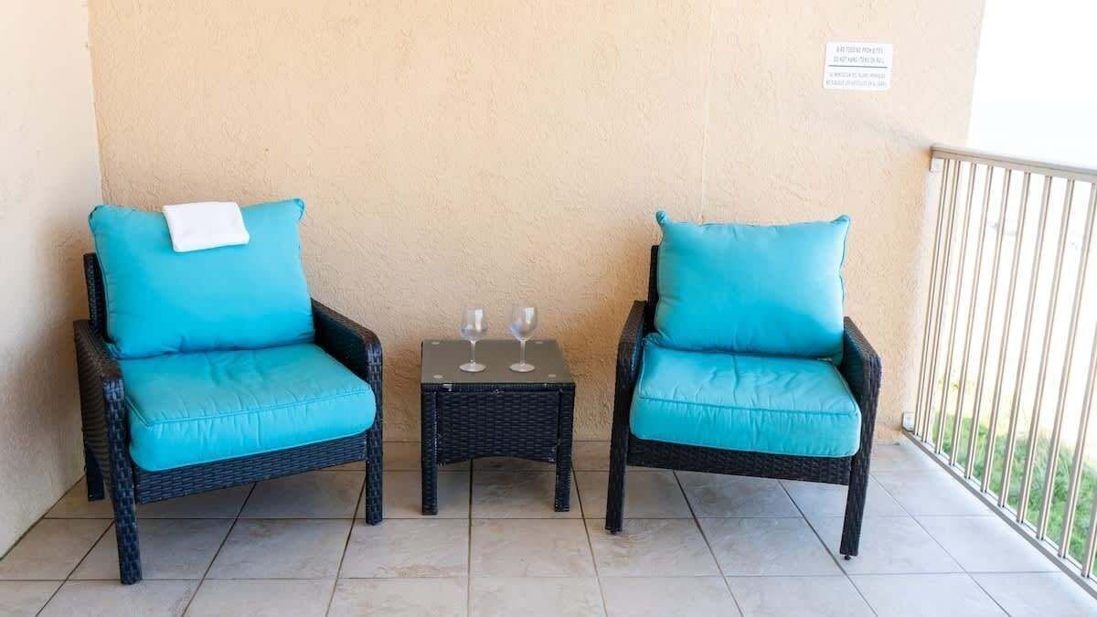 Two wicker chairs with teal cushions and a small table with two wine glasses.