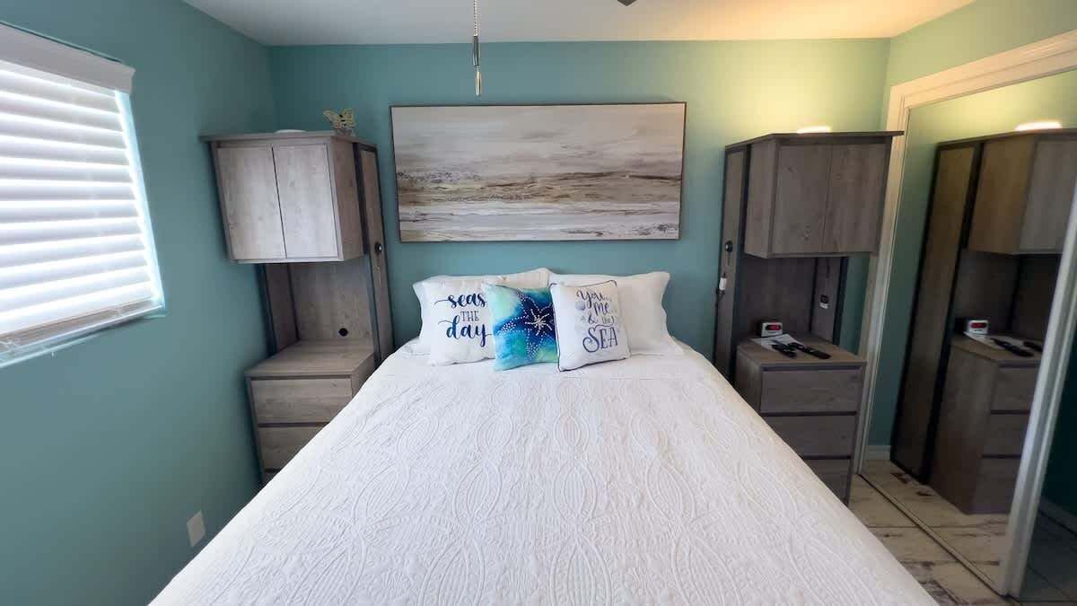 Une chambre à coucher comprenant un lit, deux tables de chevet, une grande œuvre d’art accrochée au mur et une armoire.