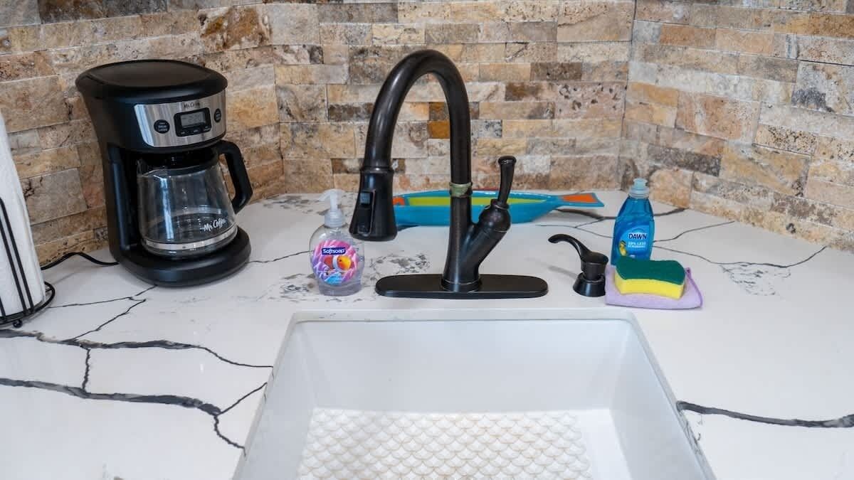 Una cocina con cafetera, grifo y productos de limpieza.