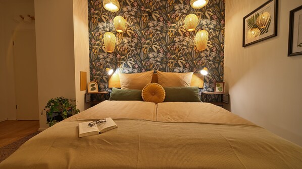 Una cama bien hecha con un libro y gafas encima, un papel tapiz floral y dos lámparas de noche.