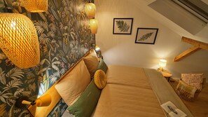 Un dormitorio acogedor con cama, almohadas, una mesita de noche y una pared decorada con hojas enmarcadas.