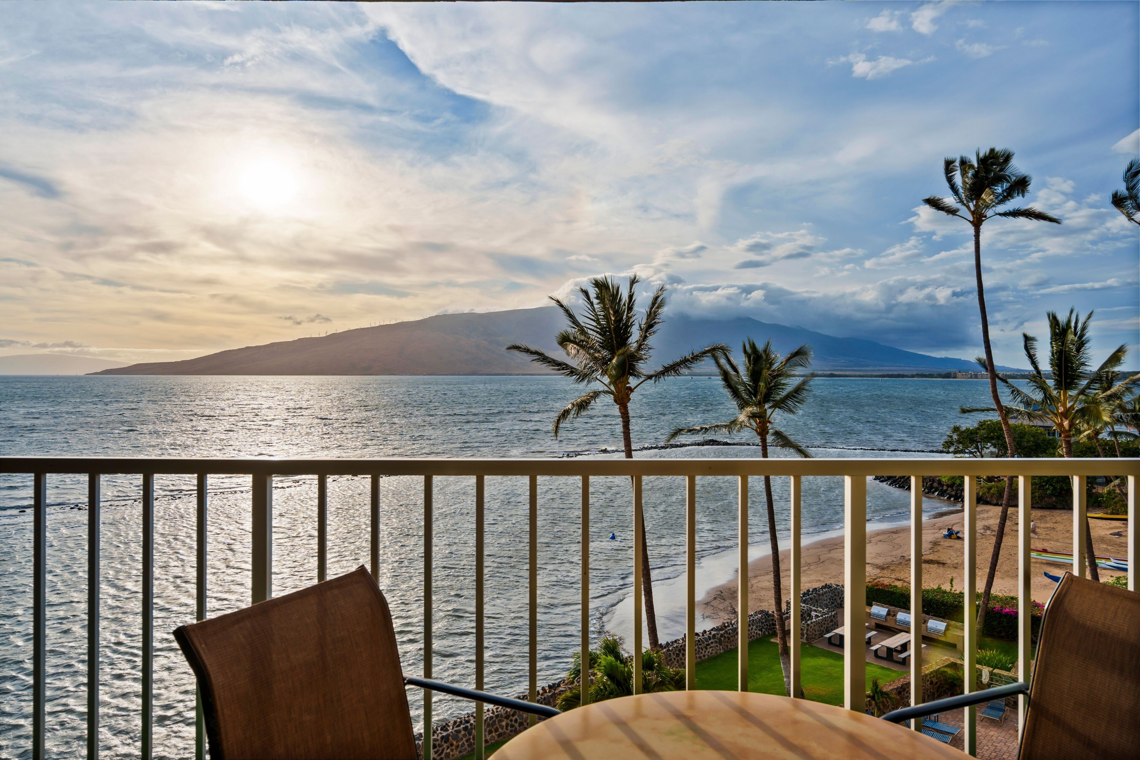 A balcony with a view of the sea, palm trees, and a distant mountain.