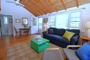 En stue med træloft, blå sofa, grønt sofabord og et spiseområde med træstole og et bord.