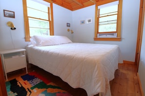 A bedroom with a bed, a nightstand, a colorful rug, and two windows.