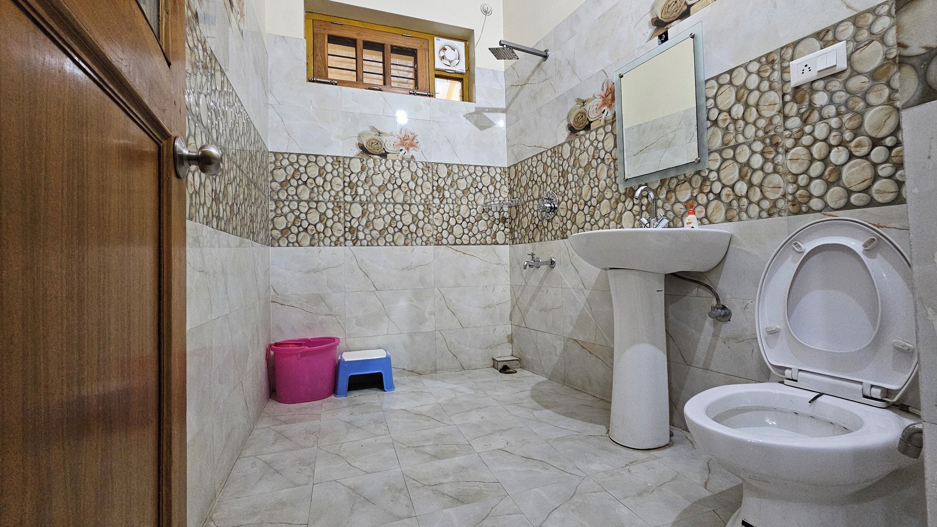 A bathroom with a toilet, sink, and shower. There is a window with wooden shutters and a stone wall.