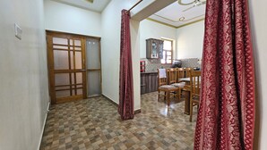 A hallway with a checkered floor leading to a dining area with wooden chairs and a table. - Bora's Homestay (Haldwani)