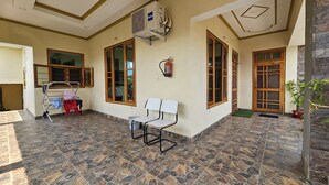 A room with a tiled floor, a ceiling fan, a fire extinguisher, and a window with wooden frames. - Bora's Homestay (Haldwani)