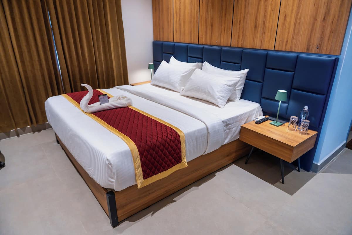 A hotel room with a bed, wooden headboard, bedside table, and a nightstand with a lamp and water bottle.