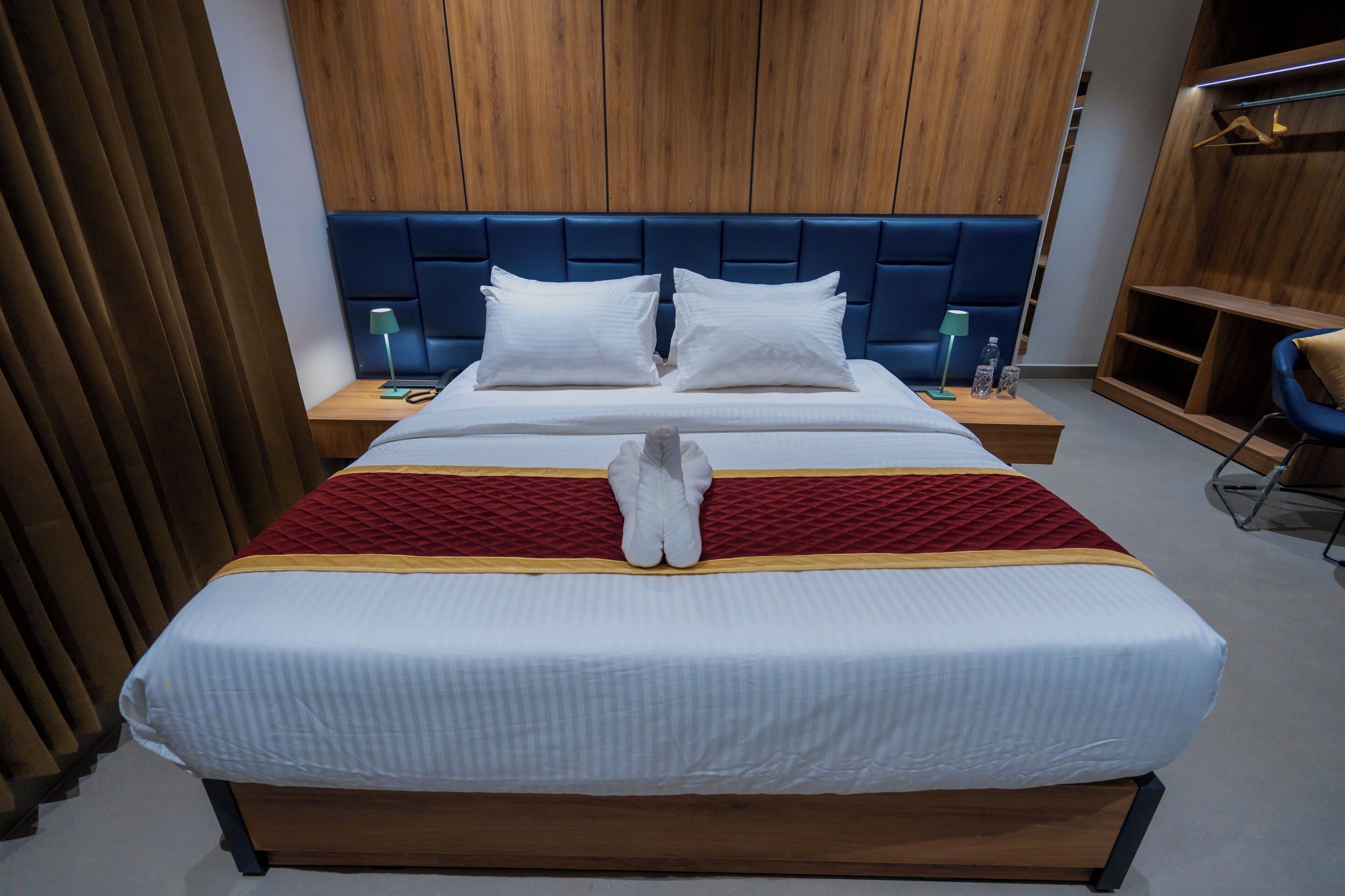 A neatly made bed with a red and white bedspread, two white pillows, and a wooden headboard. There are two bedside tables with lamps and a small shelf.
