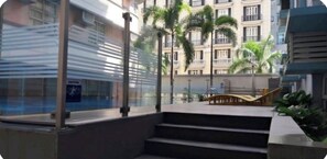 A modern building with a glass facade, outdoor stairs, and palm trees. -  Luxury cozy condo-near NAIA T3. (Pasay City)
