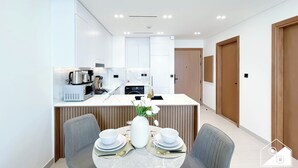 A modern kitchen with white cabinetry, a central island with appliances, and a dining area with a marble table and grey chairs. - Luxury & Comfort 1B at Binghatti Amber & Balcony (Dubai)