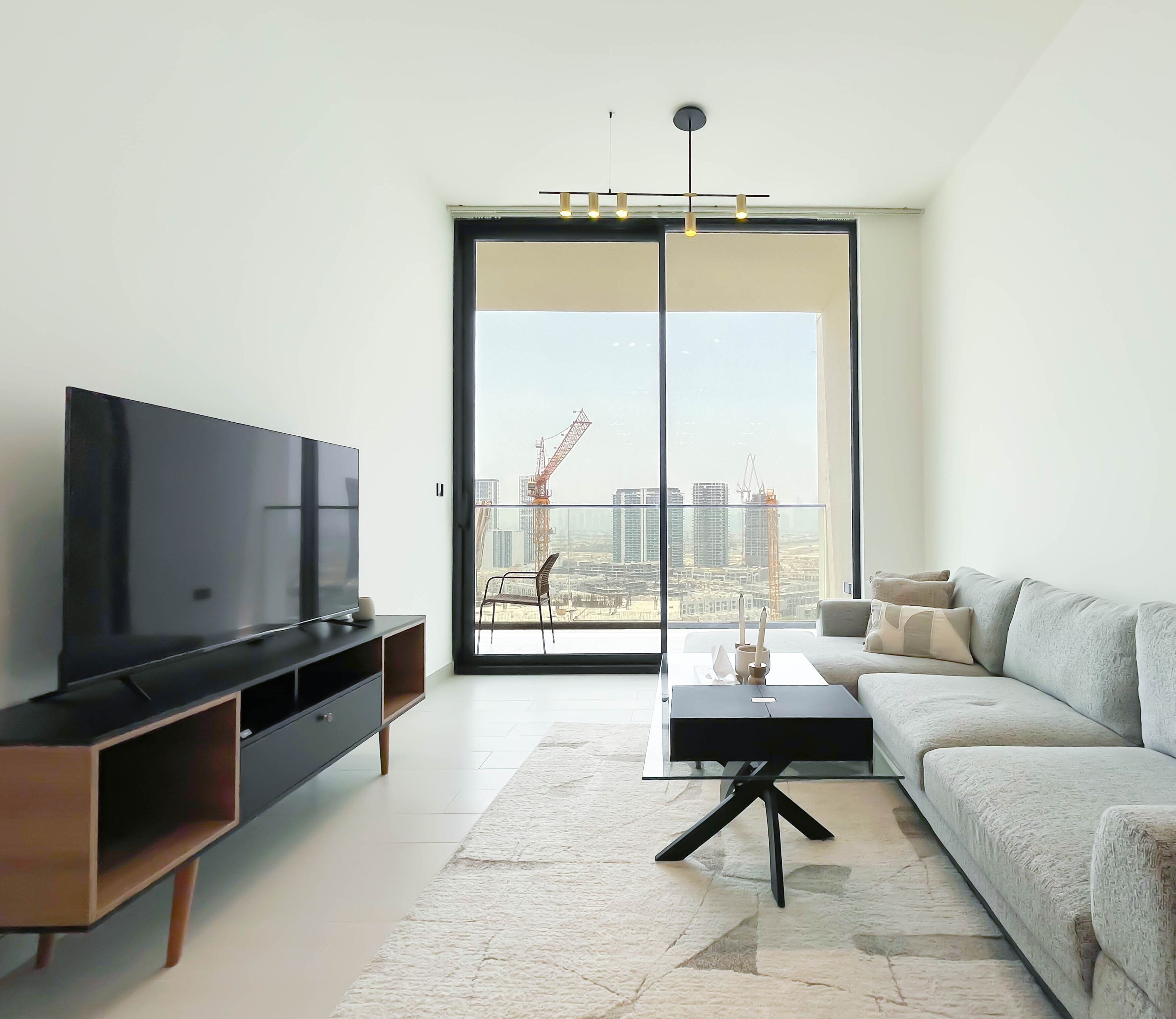 A modern living room with a flat-screen TV, a sofa, a coffee table, and a view of a construction site through large windows.