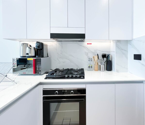 A modern kitchen with white cabinetry, a built-in microwave, a coffee maker, a gas stove, and a dishwasher. - Luxury & Comfort 1B at Binghatti Amber & Balcony (Dubai)