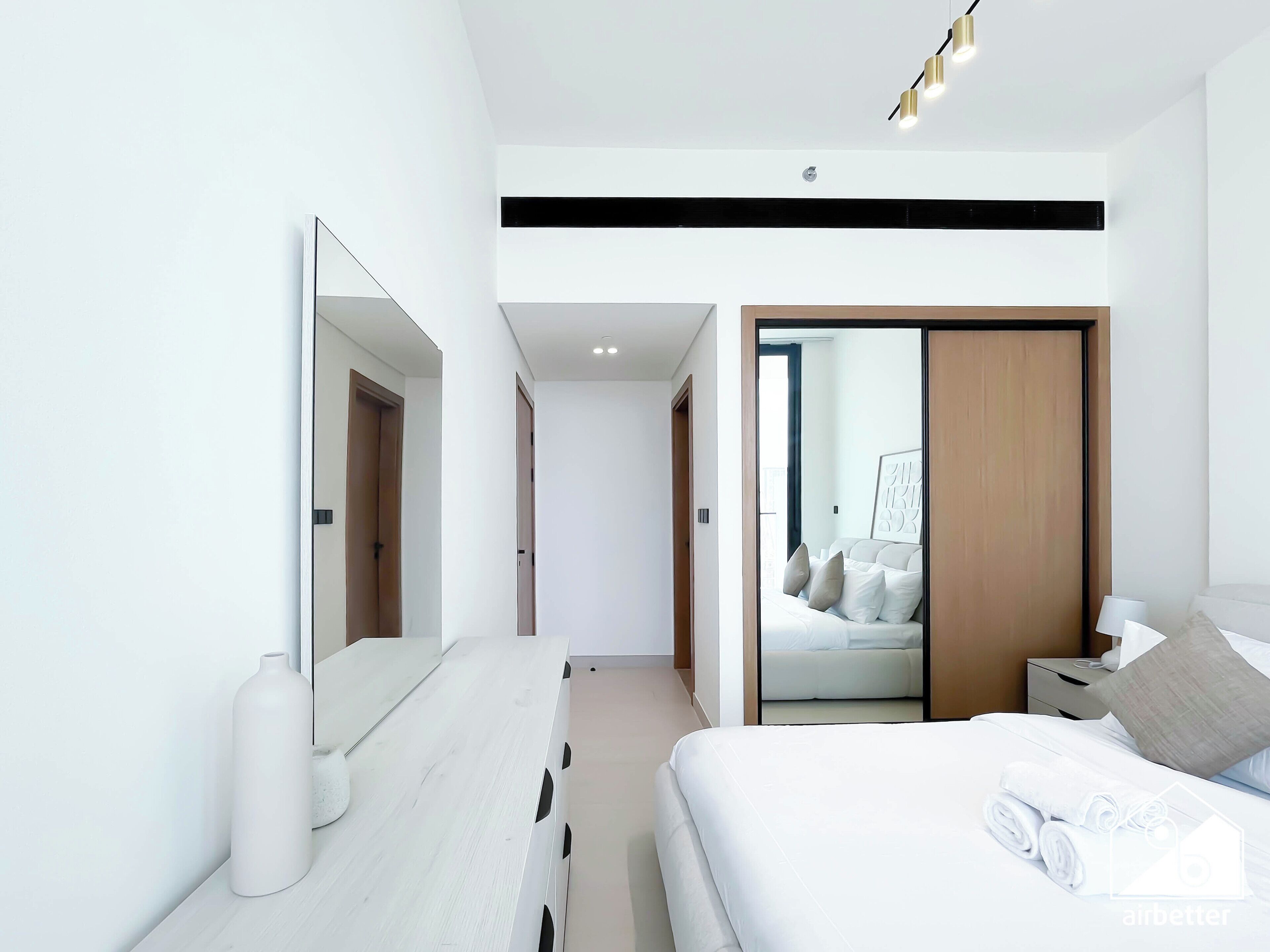 A modern hotel room with a large bed, a bedside table, a mirror, and a wardrobe.