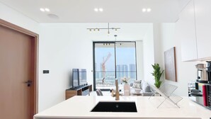A modern kitchen with a central island, a dining area with a view, and a large window. - Luxury & Comfort 1B at Binghatti Amber & Balcony (Dubai)