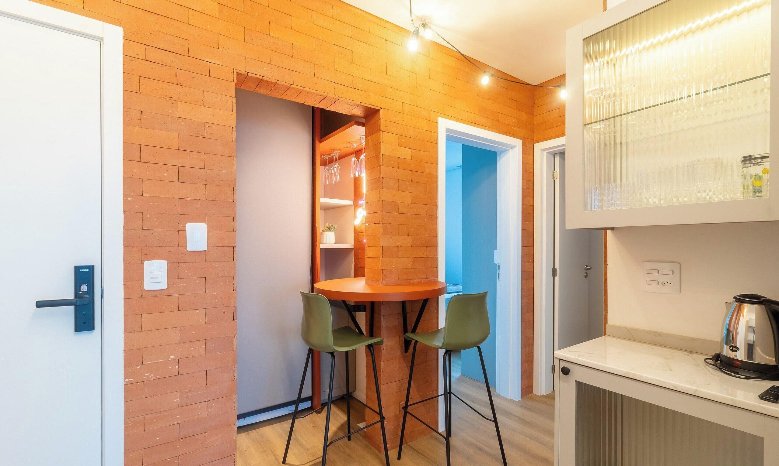 A compact kitchen with a brick wall, a small dining area with two chairs, and a coffee machine.
