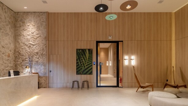 A modern reception area with a stone wall, wooden paneling, a reception desk, a seating area with a hammock, and a door leading to a hallway.