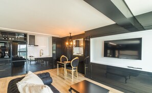Una sala de estar moderna con un sofá, una mesa de centro y una zona de comedor con sillas y una mesa. Un televisor de pantalla plana grande está montado en la pared.