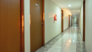 Un pasillo con puertas de madera, un extintor en la pared y suelo de baldosas.