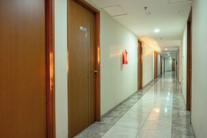 A corridor with wooden doors, a fire extinguisher mounted on the wall, and a tiled floor.