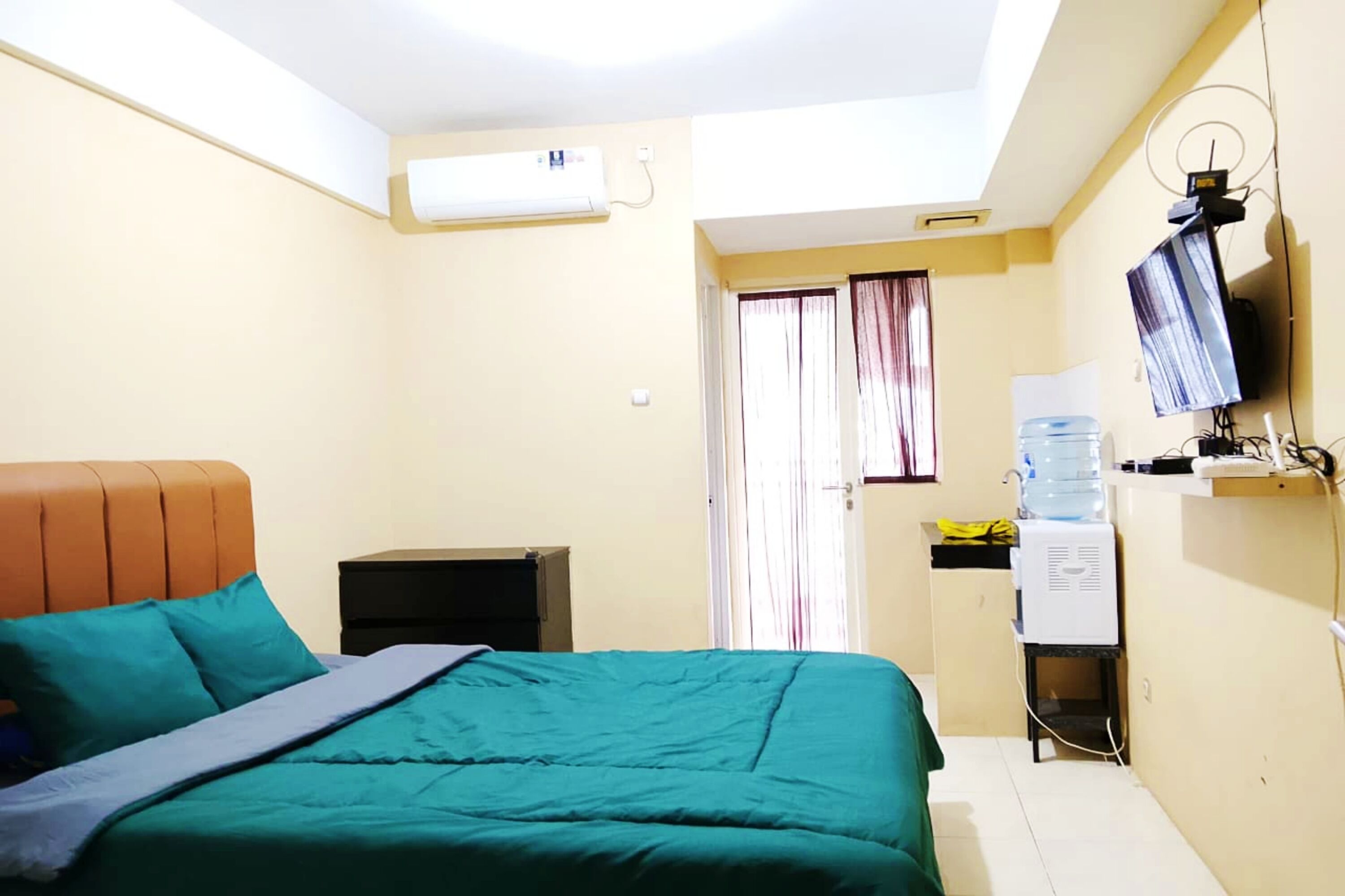 Une chambre équipée d’un lit, d’un bureau, d’un climatiseur, d’un distributeur d’eau et d’un téléviseur.