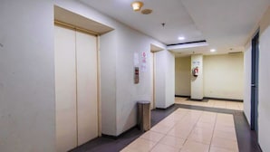 Un pasillo con suelo de baldosas, un cubo de basura y un extintor en la pared.