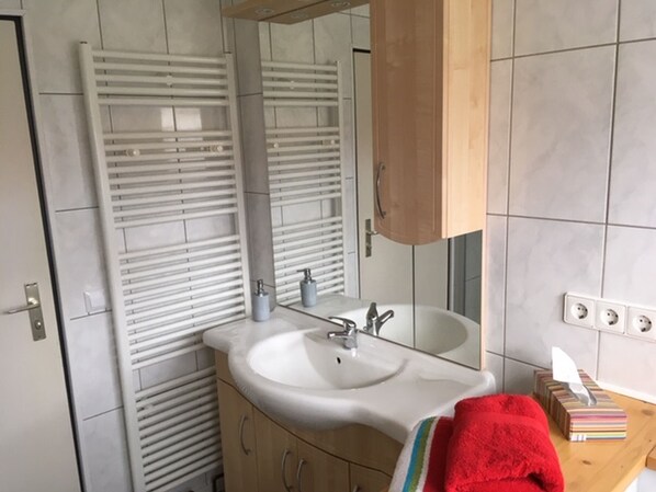 Un baño con lavabo blanco, espejo y perchero para toallas.