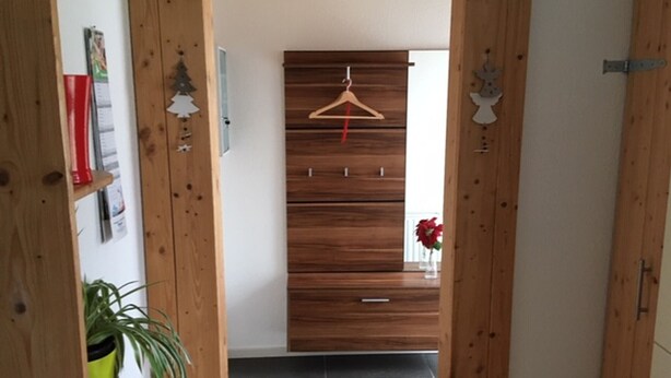 Un pasillo de madera con un perchero, una planta en maceta y una puerta que da a una habitación.