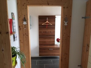 Un pasillo de madera con un perchero, una planta en maceta y una puerta que da a una habitación.