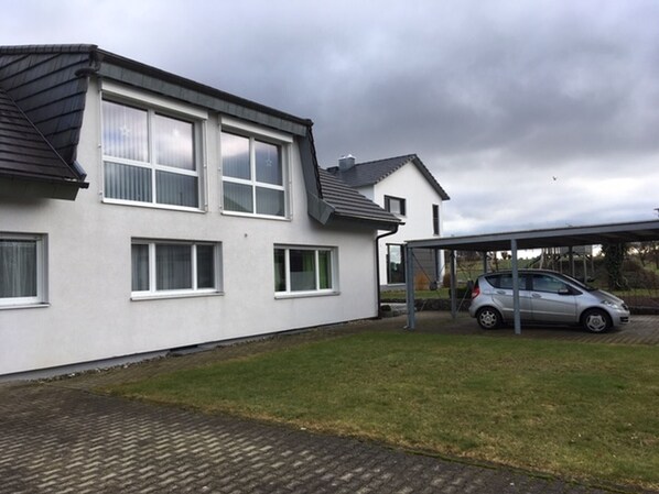 Een woonhuis met twee verdiepingen, een autoportaal en een geparkeerde auto.