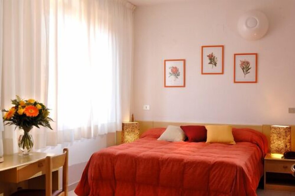 A hotel room with a bed, a desk, and a chair. There are three framed pictures on the wall.