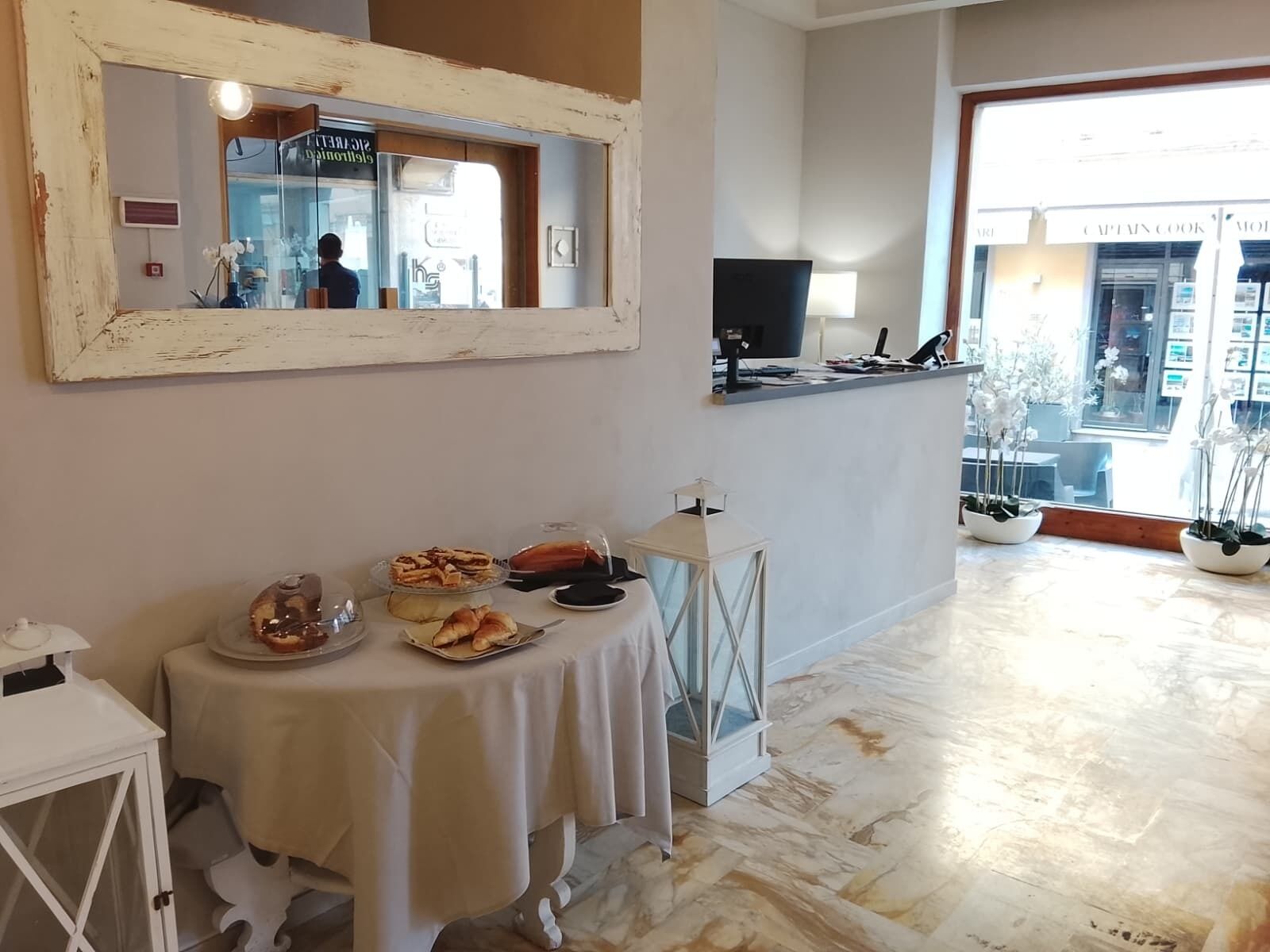 Una habitación con una mesa de comedor dispuesta con comida, un espejo grande y vista a la calle.