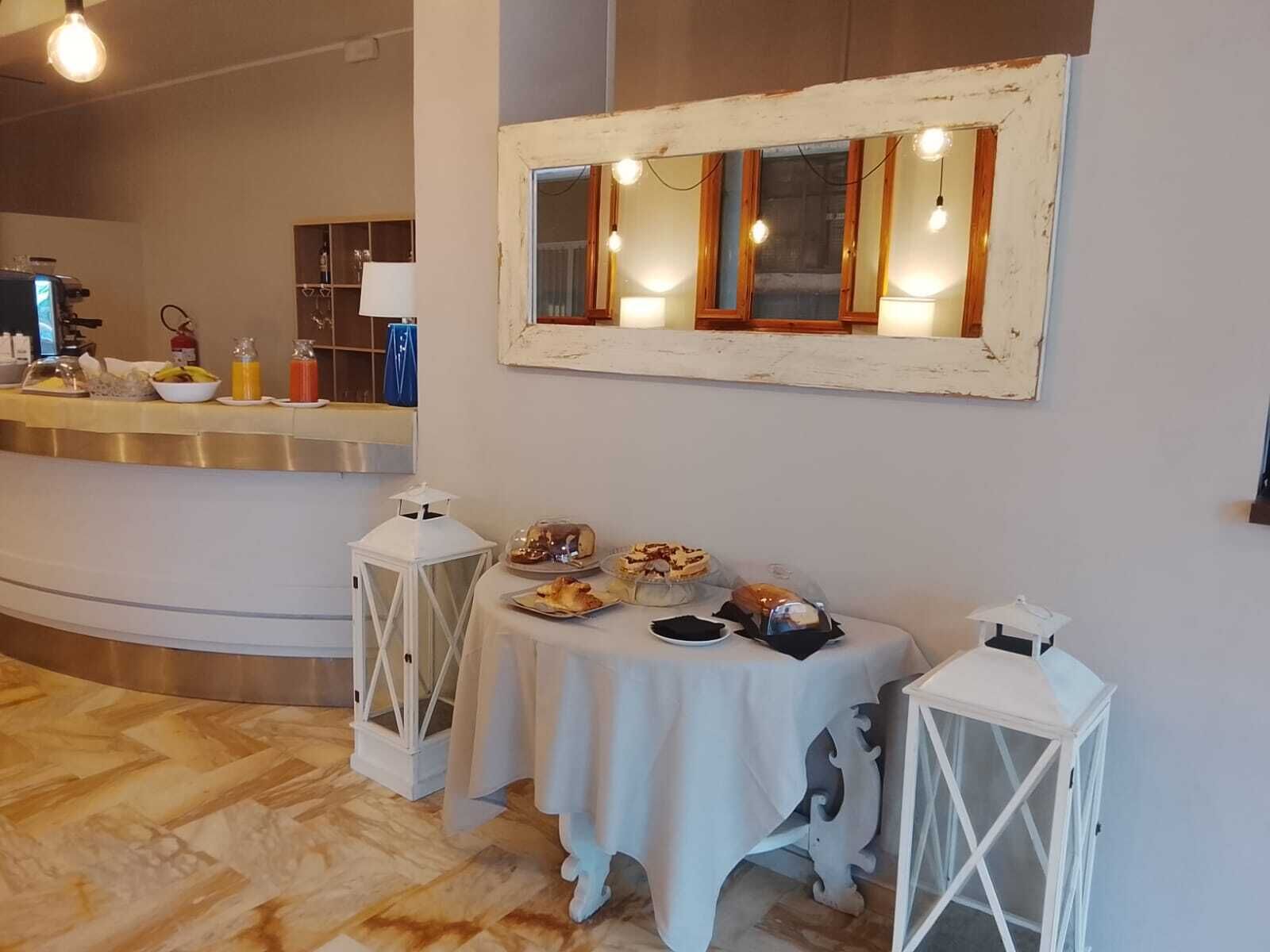 A dining area with a table set for a meal, a mirror on the wall, and a counter with kitchen appliances in the background.