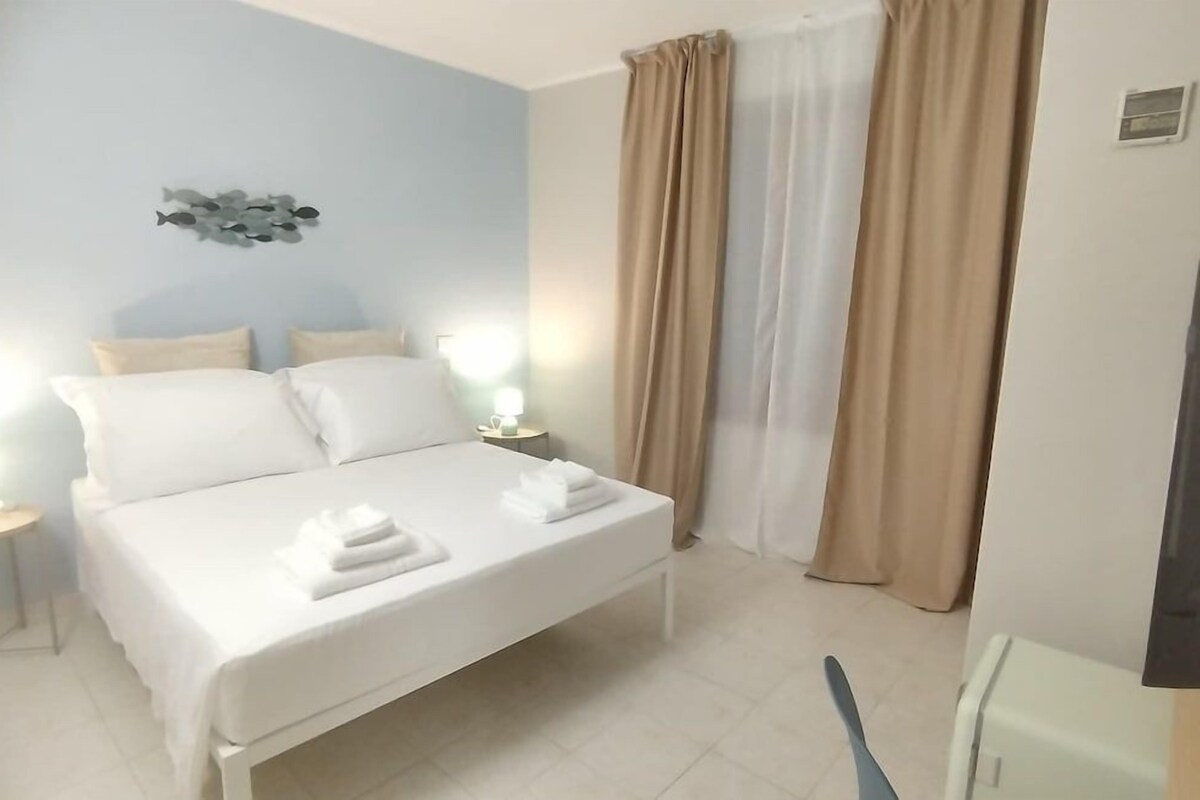 A hotel room with a bed, two bedside tables, a wall-mounted light fixture, and a television.