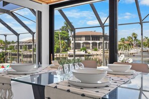 A dining area with a glass table, white plates, and clear glass vases.