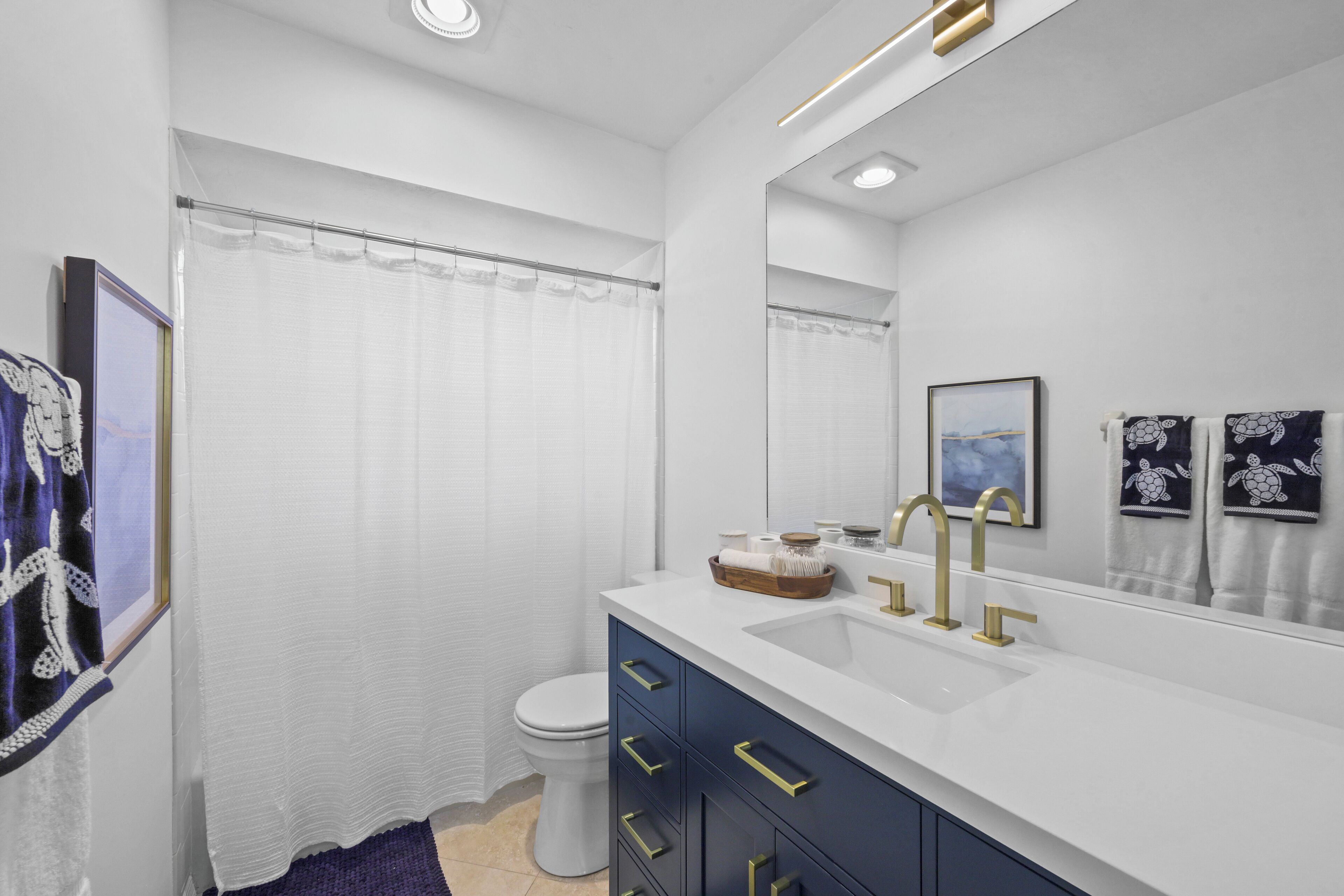 Un baño moderno con lavamanos blanco, grifos dorados y un espejo grande.