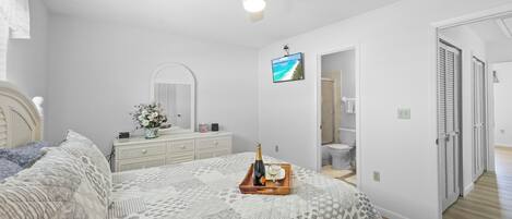 Een slaapkamer met een bed, een kapstok, een televisie en een deur naar een badkamer.