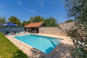 Piscina com espreguiçadeiras, área de churrasco e um muro de pedra.