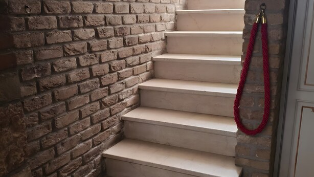 Un escalier aux marches de couleur beige, un mur de briques et une corde rouge.