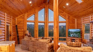 L’intérieur d’une cabane en rondins, avec une grande fenêtre, des meubles en bois et un téléviseur.