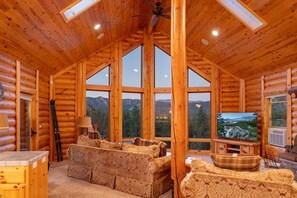 A log cabin interior with a large window, wooden furniture, and a television. - Luxury Log Cabin | Panoramic Views, Game Room, 2 Fireplaces & Outdoor Kitchen (Big Bear City)