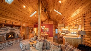 L’intérieur d’une cabane en rondins, avec une cheminée en pierre, des meubles en bois et un coin cuisine.