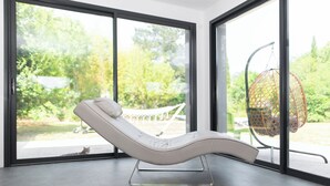 A modern room with a reclining chair, large windows, and a hanging chair.