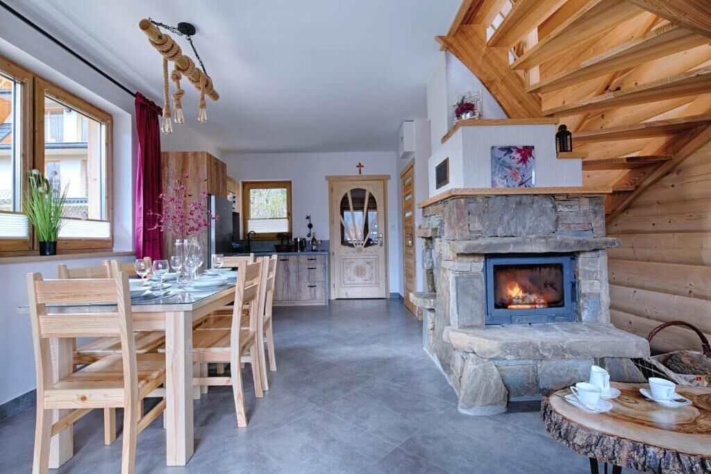 A cozy log cabin interior with a stone fireplace, wooden dining table, and chairs.