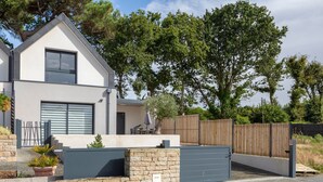 A modern two-story house with a garage, stone wall, and a wooden fence. - Modern holiday home with private terrace, Wi-Fi, and air conditioning (Fouesnant)