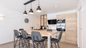 A modern kitchen with a dining area, featuring a wooden table, black chairs, and pendant lighting. - Modern holiday home with private terrace, Wi-Fi, and air conditioning (Fouesnant)