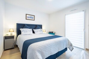 A bedroom with a bed, nightstands, a lamp, a picture on the wall, and a window with blinds.