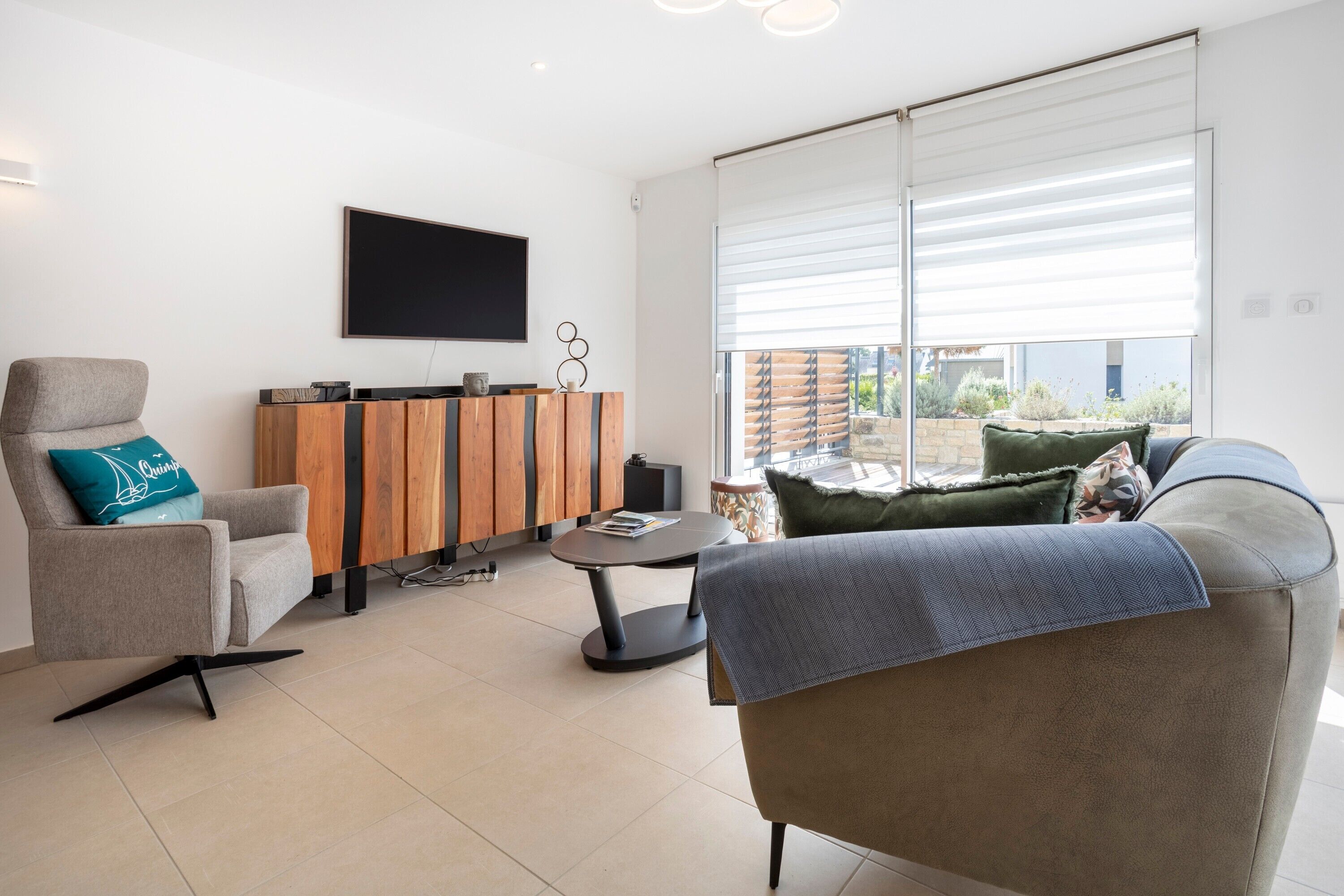 Een moderne woonkamer met een bank, fauteuil, salontafel, televisie en een houten kast.